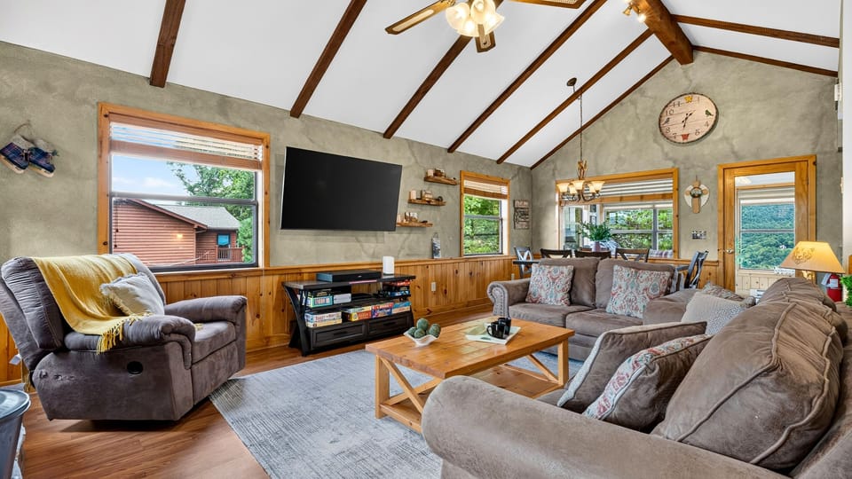 Open-concept living room with vaulted wood ceilings, stone fireplace, and comfortable sofas.