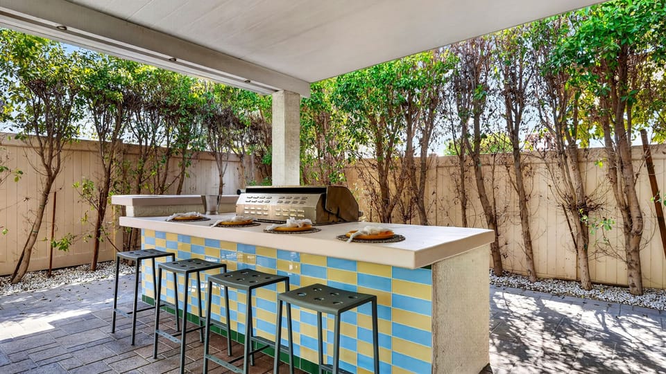 Fully equipped covered outdoor bar area with high-top seating and built-in barbecue.
