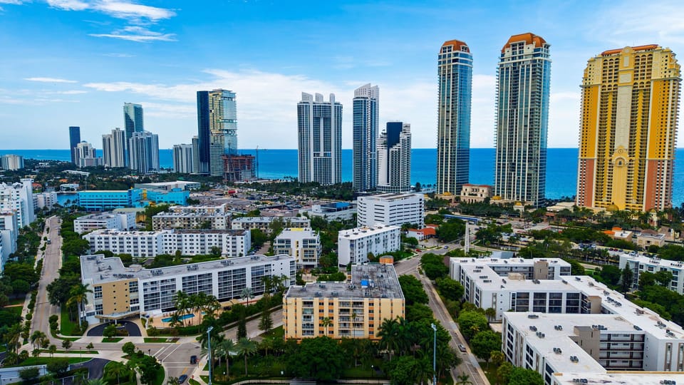 Broad aerial view highlighting Miami's skyline, blue water, and lush residential landscape.