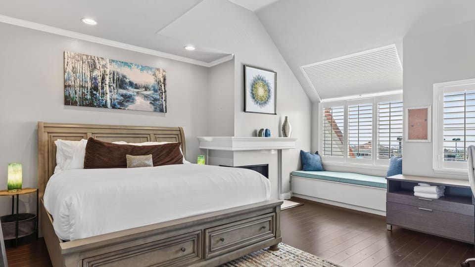 A serene primary suite with a plush bed, vaulted ceiling, fireplace, and built-in window seat.
