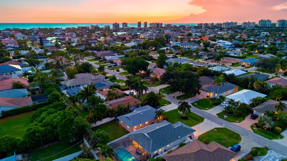 A sunset aerial places the home within a relaxed coastal neighborhood, with the Gulf and shoreline stretching across the horizon.