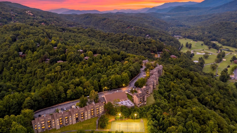 A sunset aerial reveals the resort tucked into the Smoky Mountains, with forested surroundings, tennis courts, and nearby golf scenery.