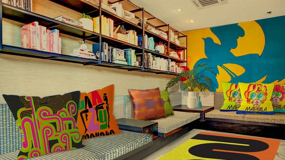 A bright queen bedroom with playful artwork, a cozy reading chair, and sunlight streaming through the windows.