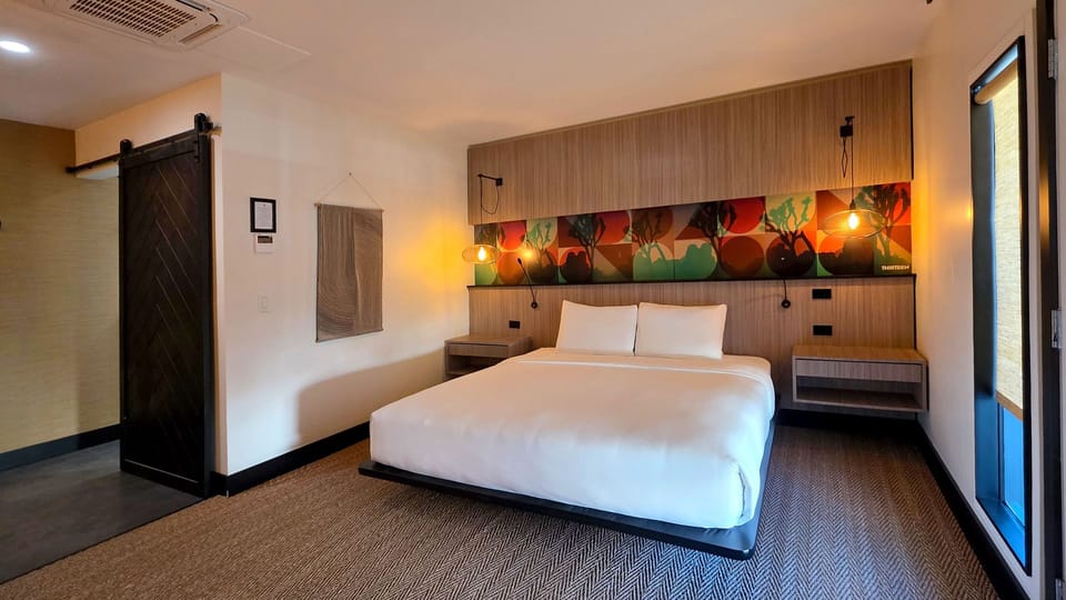 The studio bedroom features a king bed, colorful artwork, warm pendant lighting, and playful modern design.