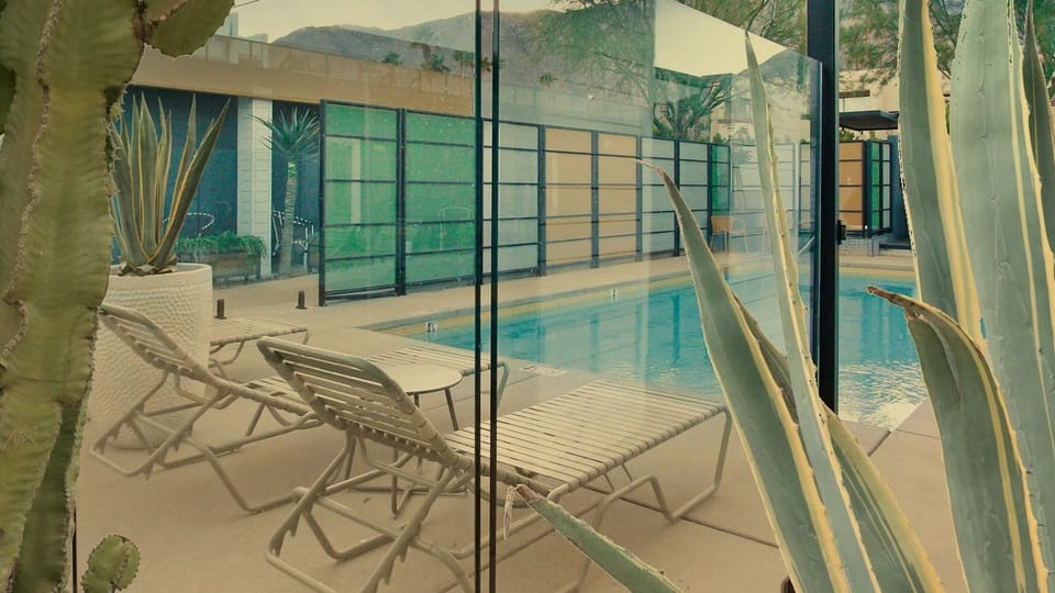 A bright pool entrance framed by palms, loungers, and colorful resort-style design.