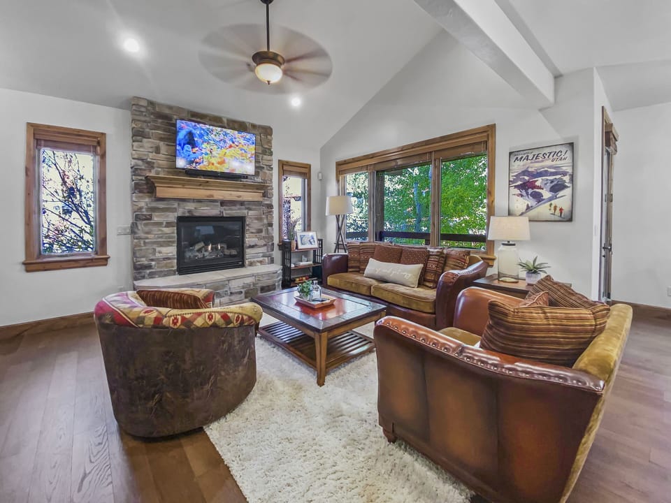 This cozy mountain lounge features a warm stone fireplace, plush seating, and vaulted ceilings. Relax with a movie or enjoy the natural light from large windows overlooking the trees.