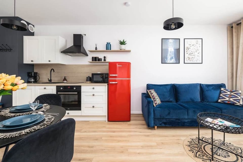 An open-plan living space combining a kitchen with white cabinets, a red retro-style fridge, and a blue sofa.
