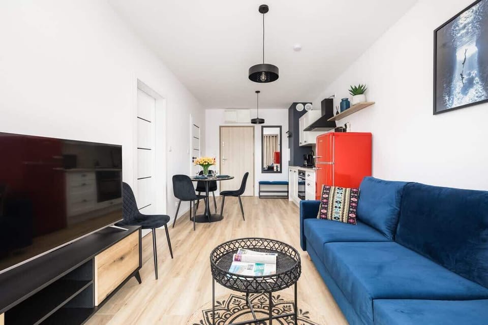 A TV area with a sleek wooden cabinet, a blue sofa, and a spacious, well-lit interior.
