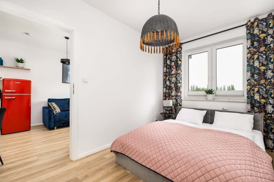 A view of the bedroom leading into the open-plan living space, featuring the red fridge and blue sofa.
