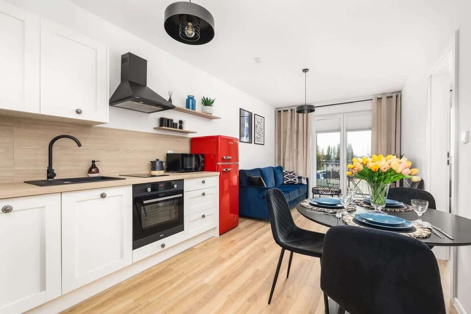 A kitchen with white cabinets, a black countertop, and a bold red fridge as a statement piece.
