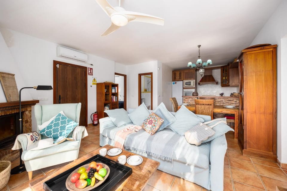 Open-plan living room with sofa, dining area, kitchen, ornamental fireplace, A/C, WiFi internet, and satellite TV