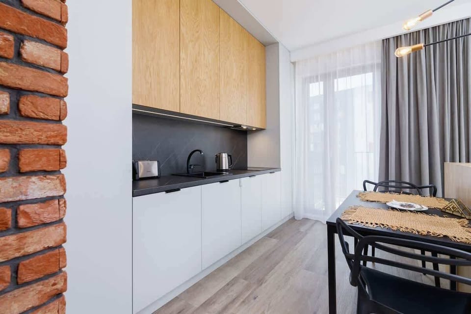 The kitchen area with light wood cabinets and black countertops. A small dining table is visible, emphasizing the compact, efficient layout.
