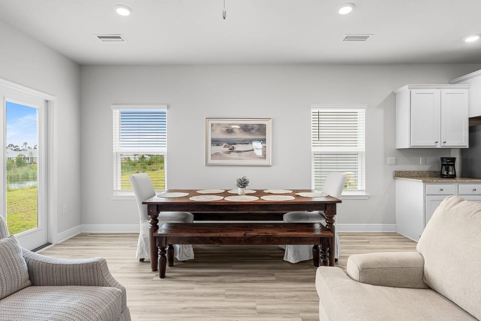 Gather around this beautiful dining table where coastal artwork and bright windows create the perfect setting for your memorable meals together.