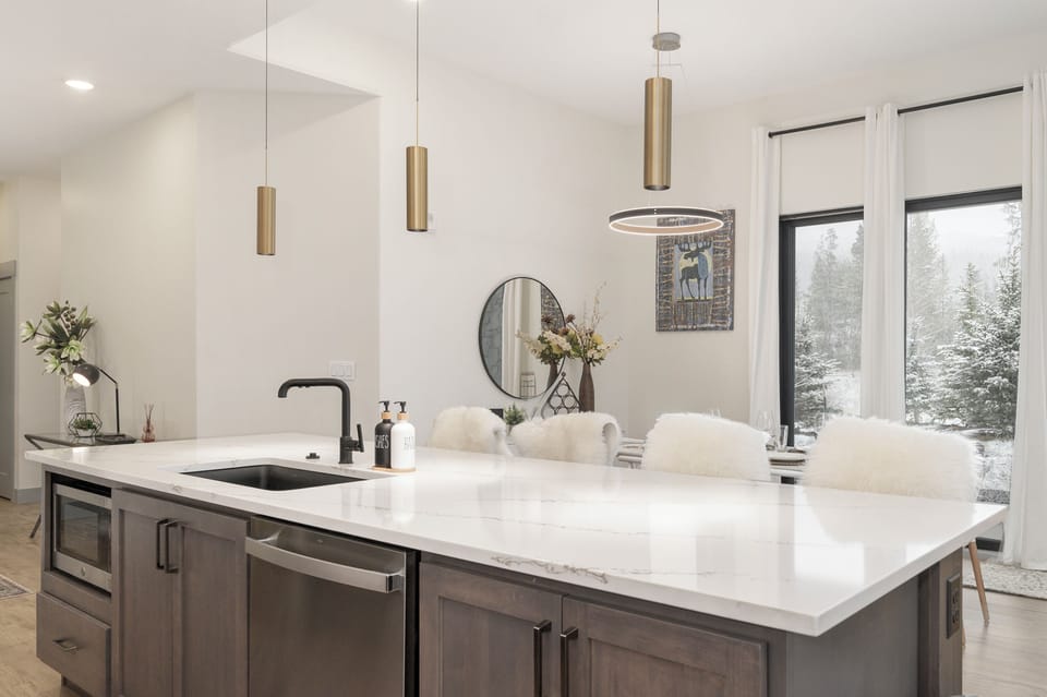 Cook with inspiration in this modern kitchen featuring sleek marble counters, pendant lighting, and winter forest views.