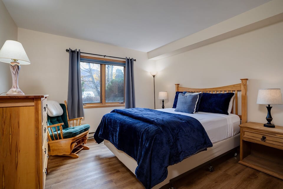 Sink into crisp white linens and plush navy bedding in your peaceful bedroom, where warm wood tones create a cozy retreat.