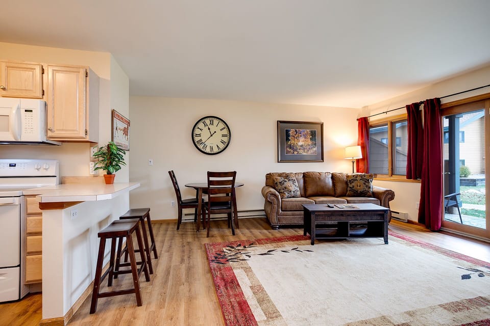 Relax in your open-concept living space with cozy leather seating, fully equipped kitchen, and warm natural light streaming through large windows.