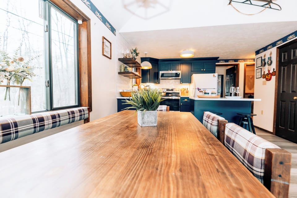 Farmhouse table with plaid seating, kitchen and wooded views.