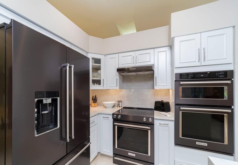 Black stainless steel refrigerator, double wall ovens, and white cabinetry with subway tile backsplash in kitchen.
