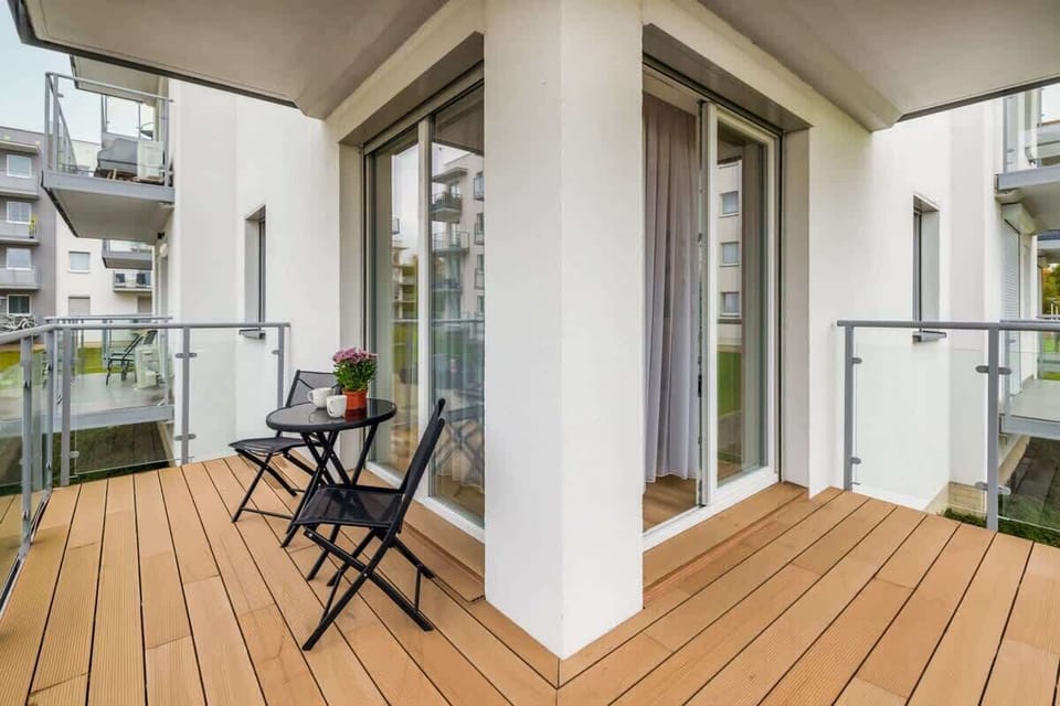 A spacious balcony with wooden flooring, two black chairs, and a small table.
