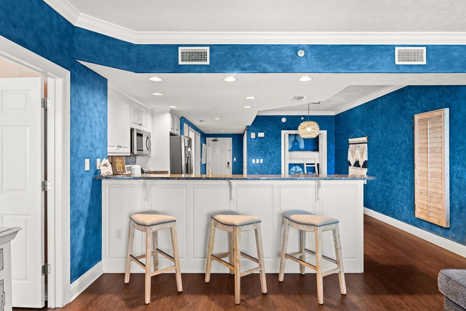Gather around your bright breakfast bar with ocean-inspired blue walls and modern white cabinetry for memorable morning conversations.