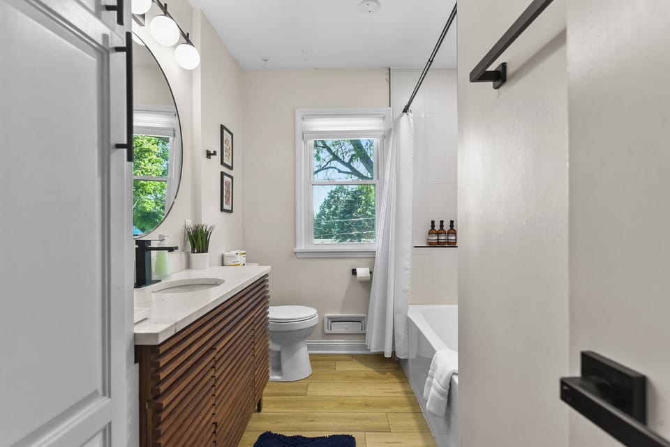 Your modern bathroom features a stylish vanity, rainfall shower, and natural light streaming through the window overlooking lush greenery.