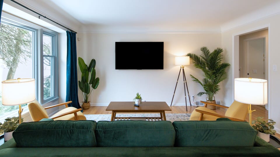 Sink into plush emerald seating while natural light fills your stylish living space, complete with modern entertainment and tropical greenery.