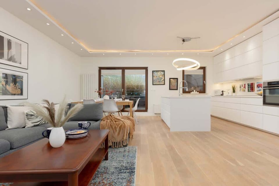 A bright open-plan living area with a sofa, rug, and a dining space next to the kitchen.
