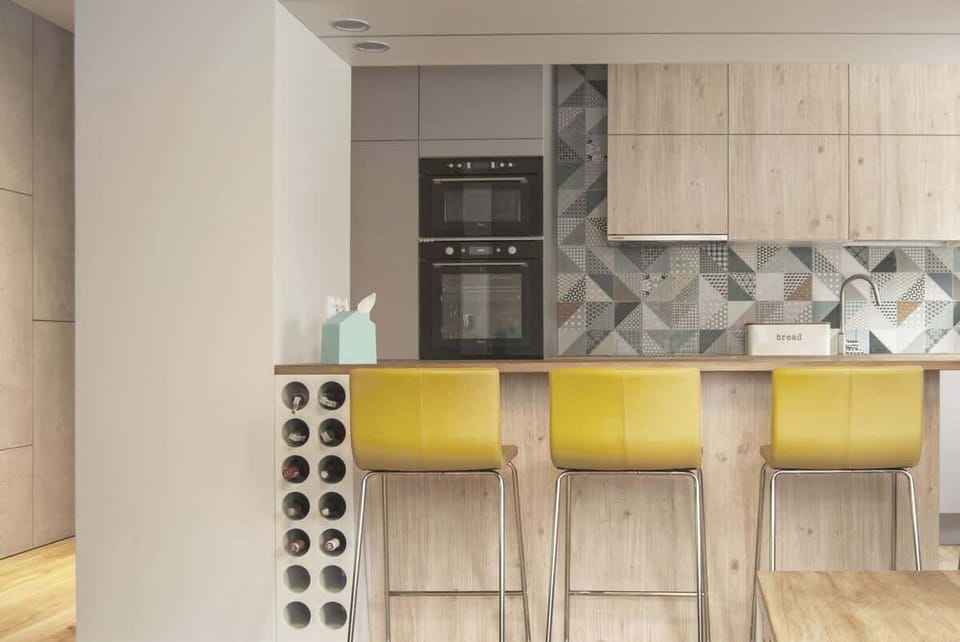 A different perspective of the kitchen, highlighting the bar stools and geometric wall tiles.
