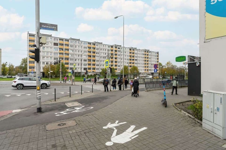 A pedestrian crossing with a bike lane, leading to residential buildings and a bus stop.
