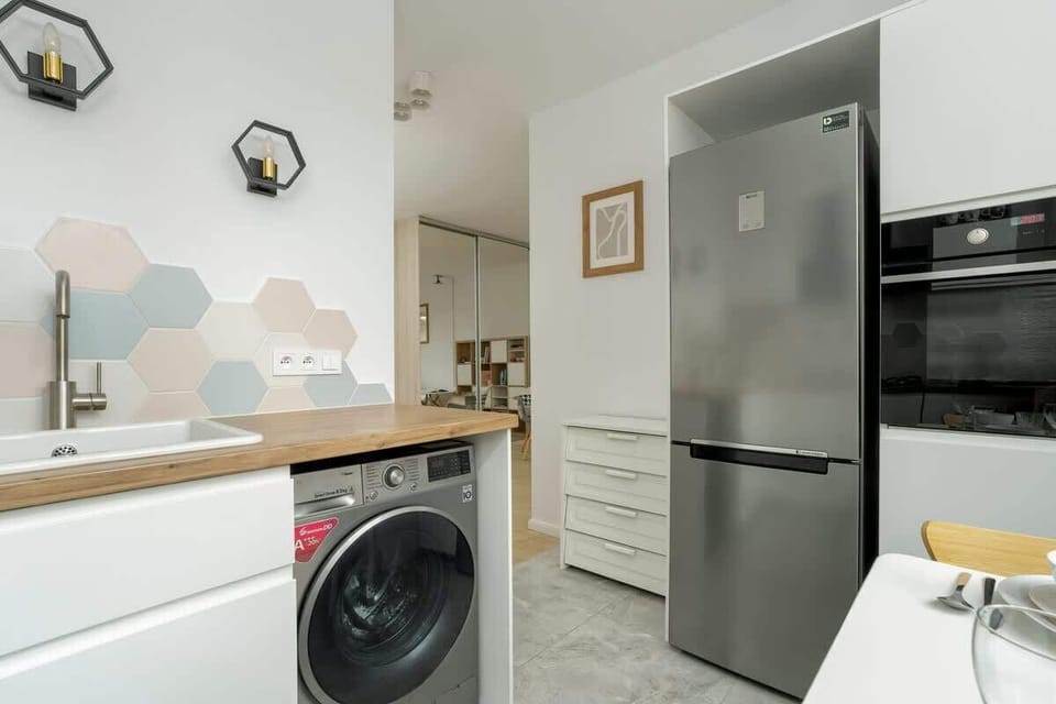 A modern kitchen with a washing machine, stainless steel refrigerator, and stylish hexagonal backsplash tiles.
