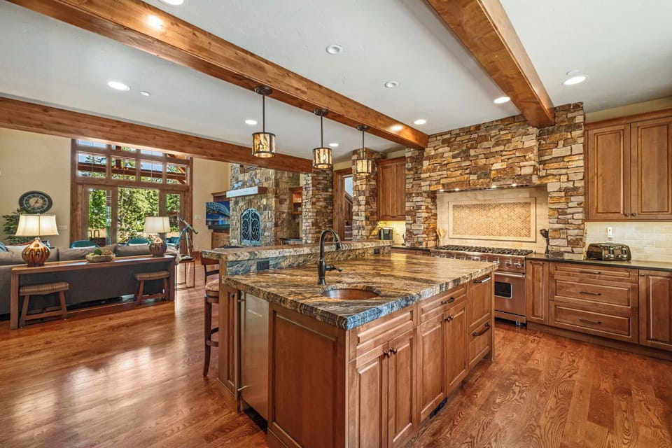 Gourmet chef’s kitchen with granite island, stone backsplash, and timber beams.
