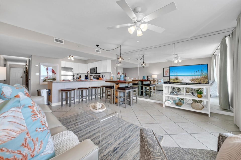 Relax in your open-concept living space with coastal touches, modern kitchen island, and beach views on the TV.