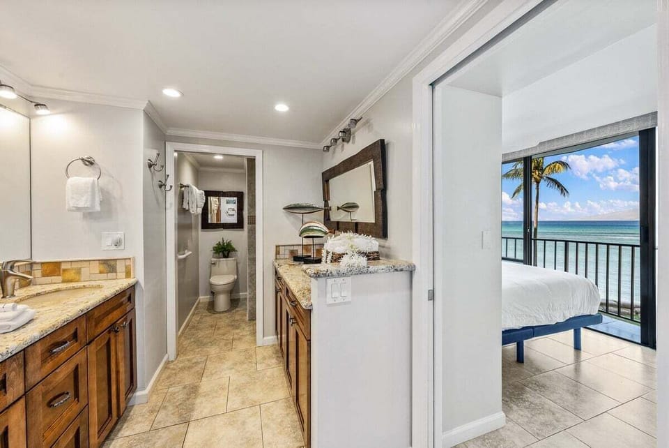Hallway leading to bathroom and ocean‑view bedroom — granite counters inside, palm‑framed horizon waiting beyond.