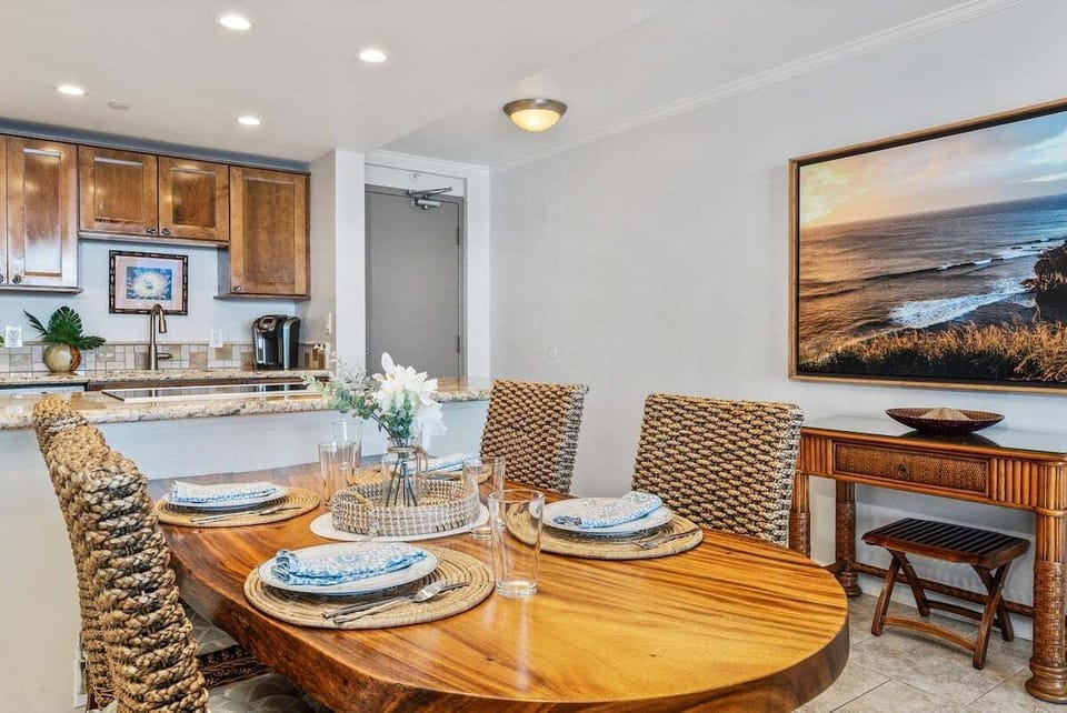 Round dining table with centerpiece and kitchen nearby — bar stools ready, coffee brewing, tropical vibes flowing through the space