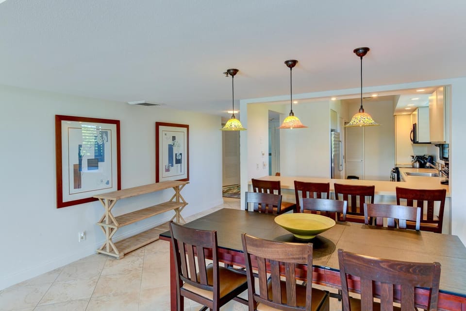 Pendant lights hang above a kitchen pass-through with a breakfast bar and four wooden chairs.