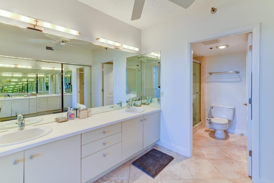 Bathroom with dual sinks set in a long white vanity, large mirrors, and a separate room for toilet and shower.