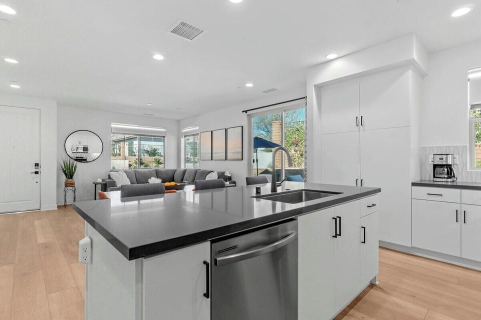 Black quartz island anchors white cabinetry—open sightlines to living room keep everyone connected.
