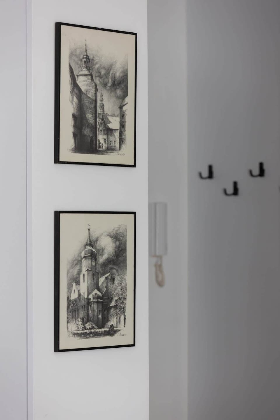 A hallway with framed black-and-white artwork, wall hooks, and a clean, minimalist aesthetic.
