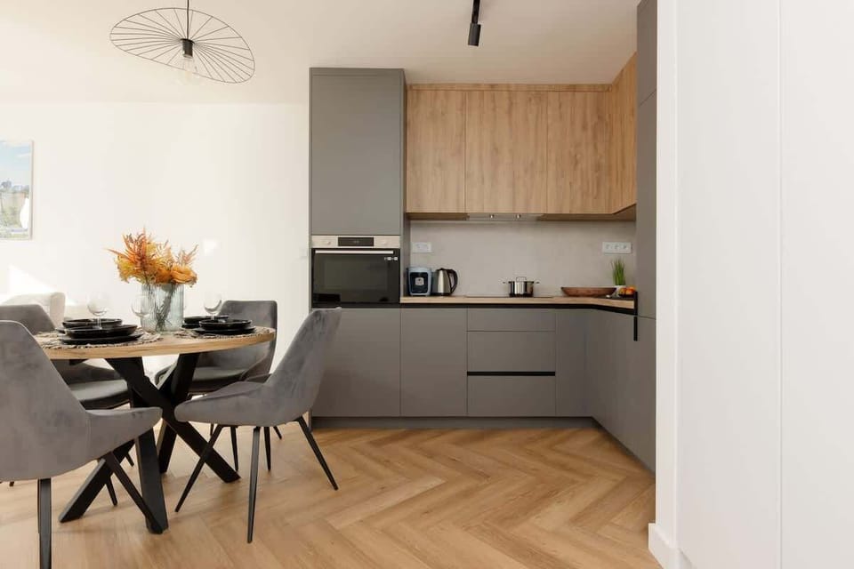 A sleek open-plan kitchen with gray cabinets, wooden accents, and a dining area with a stylish black table.
