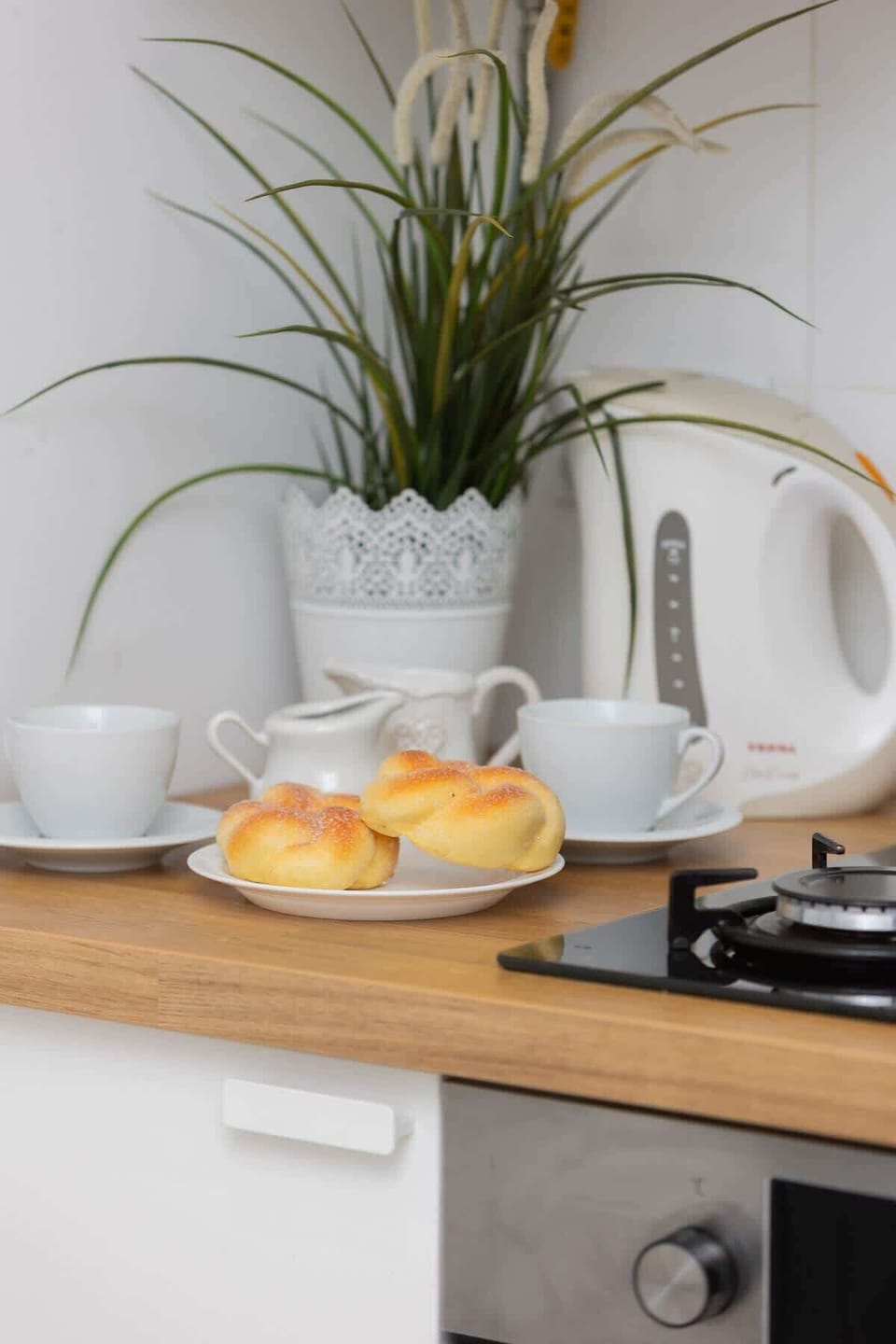A close-up of a wooden countertop with a kettle, fresh fruit, and a small plant for decoration.

