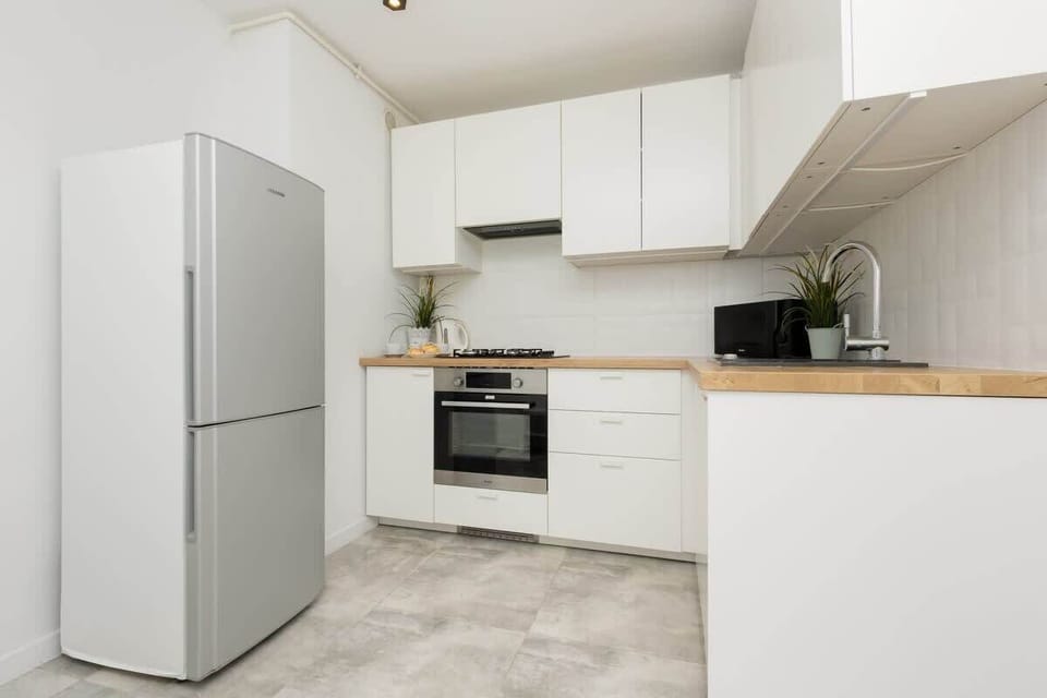 A modern kitchen with white cabinetry, a stainless steel refrigerator, and a wooden countertop.
