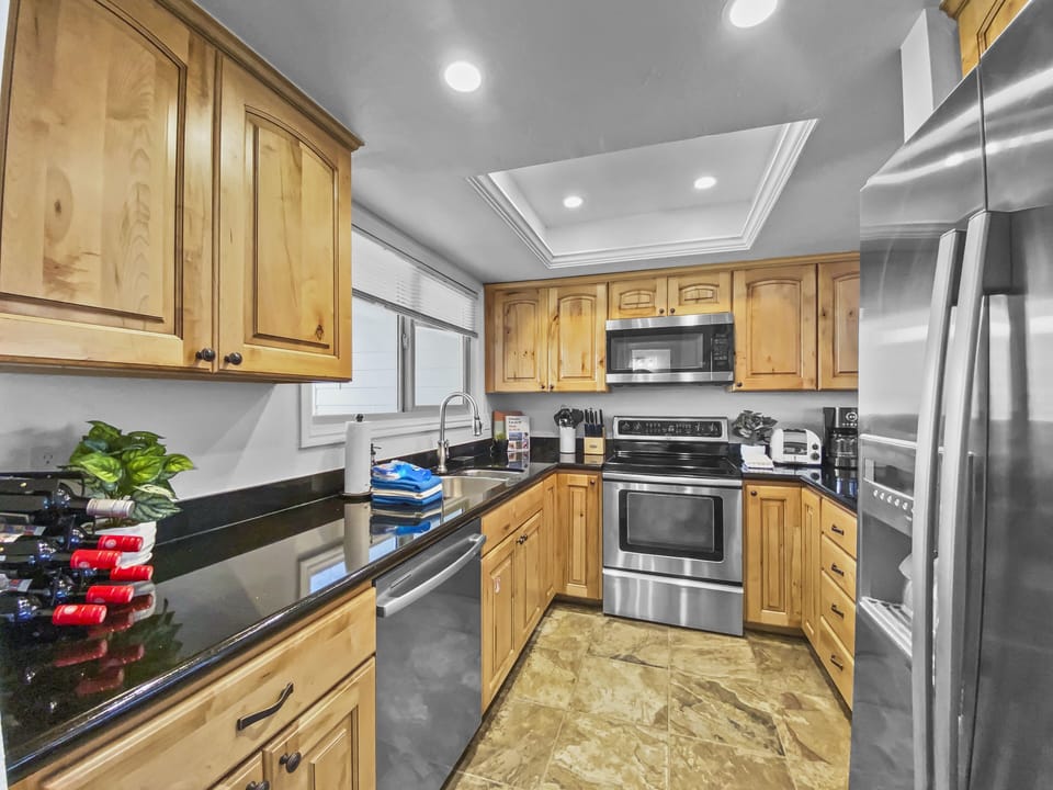 Cook with ease in this well-appointed gourmet kitchen featuring stainless steel appliances, warm wood cabinetry, and sleek black countertops—an inviting hub for group meals and morning coffee.