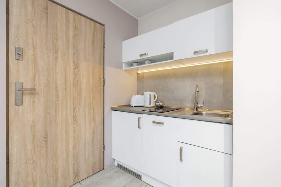 A compact kitchen with white cabinets, wooden accents, and a stainless steel kettle.

