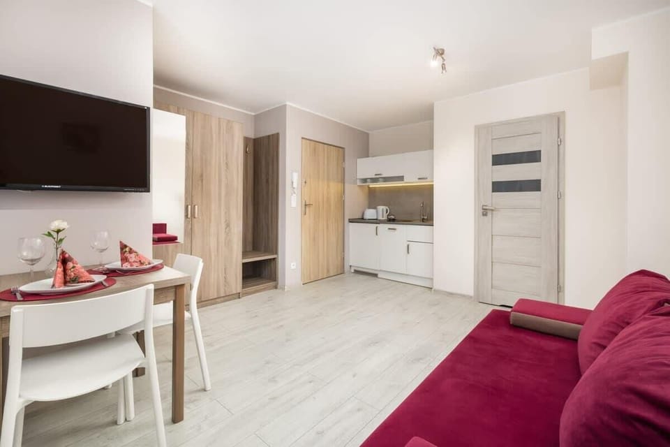 An open-plan dining and kitchen area with a small table set for two and a wall-mounted TV.

