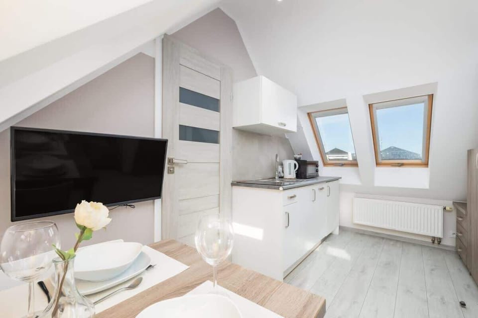 An attic living area with a small dining table, a TV, and a bright, open kitchen.


