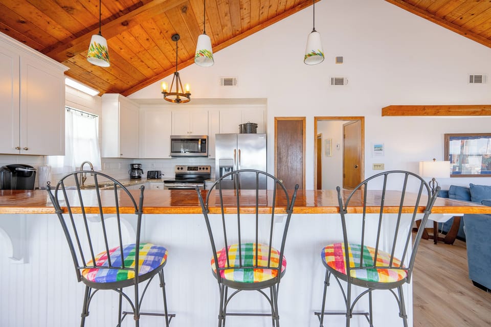 The kitchen features stainless appliances, granite countertops, and colorful bar stools, creating a vibrant, functional space