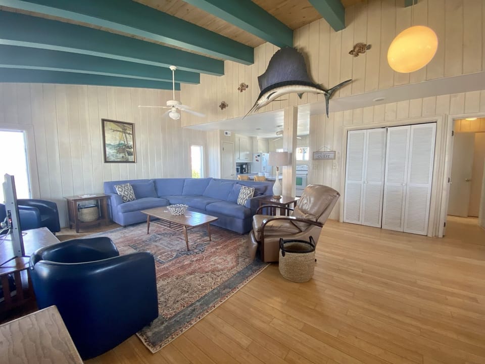 Relax in your spacious living room featuring exposed turquoise beams, coastal décor, and a cozy sectional perfect for unwinding after your adventures.