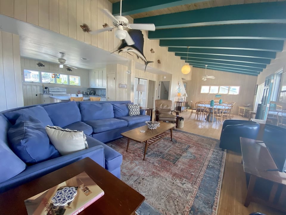 Unwind in your spacious coastal living room with plush blue sectional, exposed turquoise beams, and open kitchen—perfect for gathering after beach days.