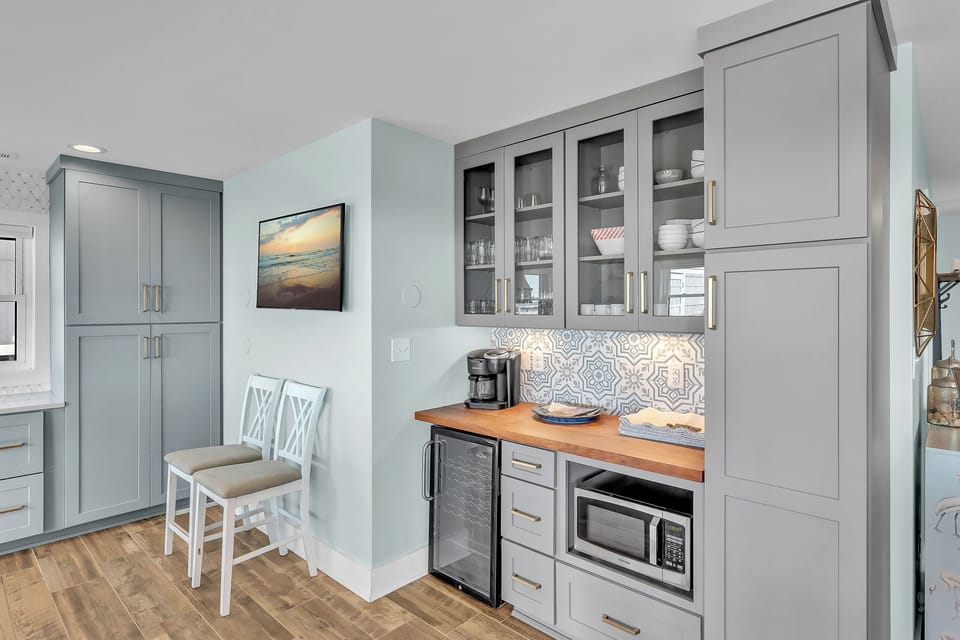 Your stylish kitchenette features everything you need - microwave, coffee maker, and elegant gray cabinetry with warm wood countertops for convenient meal prep.