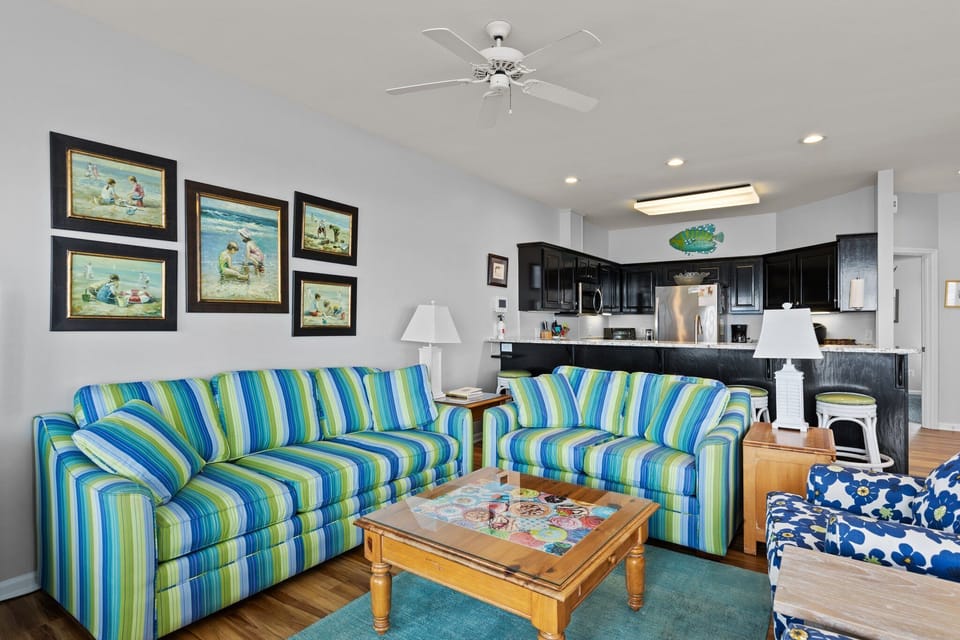 Relax in your bright, coastal-themed living space featuring vibrant striped sofas and cheerful beach artwork that brings seaside charm indoors.
